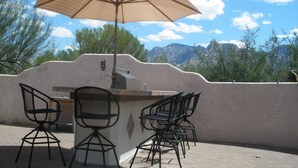 An outdoor patio with a barbecue grill, two chairs, and a large umbrella. - Piazza Rocca - private acre w/Pool, hot tub, 270 degree mountain views! (Tucson)