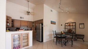 A modern kitchen with wooden cabinets, a stainless steel refrigerator, and a dining area with a table and chairs. - Piazza Rocca - private acre w/Pool, hot tub, 270 degree mountain views! (Tucson)