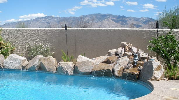 A swimming pool with a rocky edge, surrounded by a stone wall and a view of mountains. - Piazza Rocca - private acre w/Pool, hot tub, 270 degree mountain views! (Tucson)