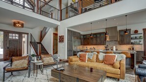 A spacious living area with a high ceiling, a staircase, and a kitchen with modern appliances. - Sunriver retreat; 5bed, 4primarysuite,Theatre rm!! (Sunriver)