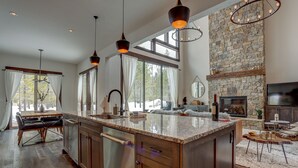 A spacious kitchen with a large island, wooden cabinets, and a stone fireplace. - Sunriver retreat; 5bed, 4primarysuite,Theatre rm!! (Sunriver)