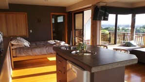 A compact bedroom with a bed, a small kitchenette, and a balcony with a view. - Beautiful Waterview Studio (Ngunguru)