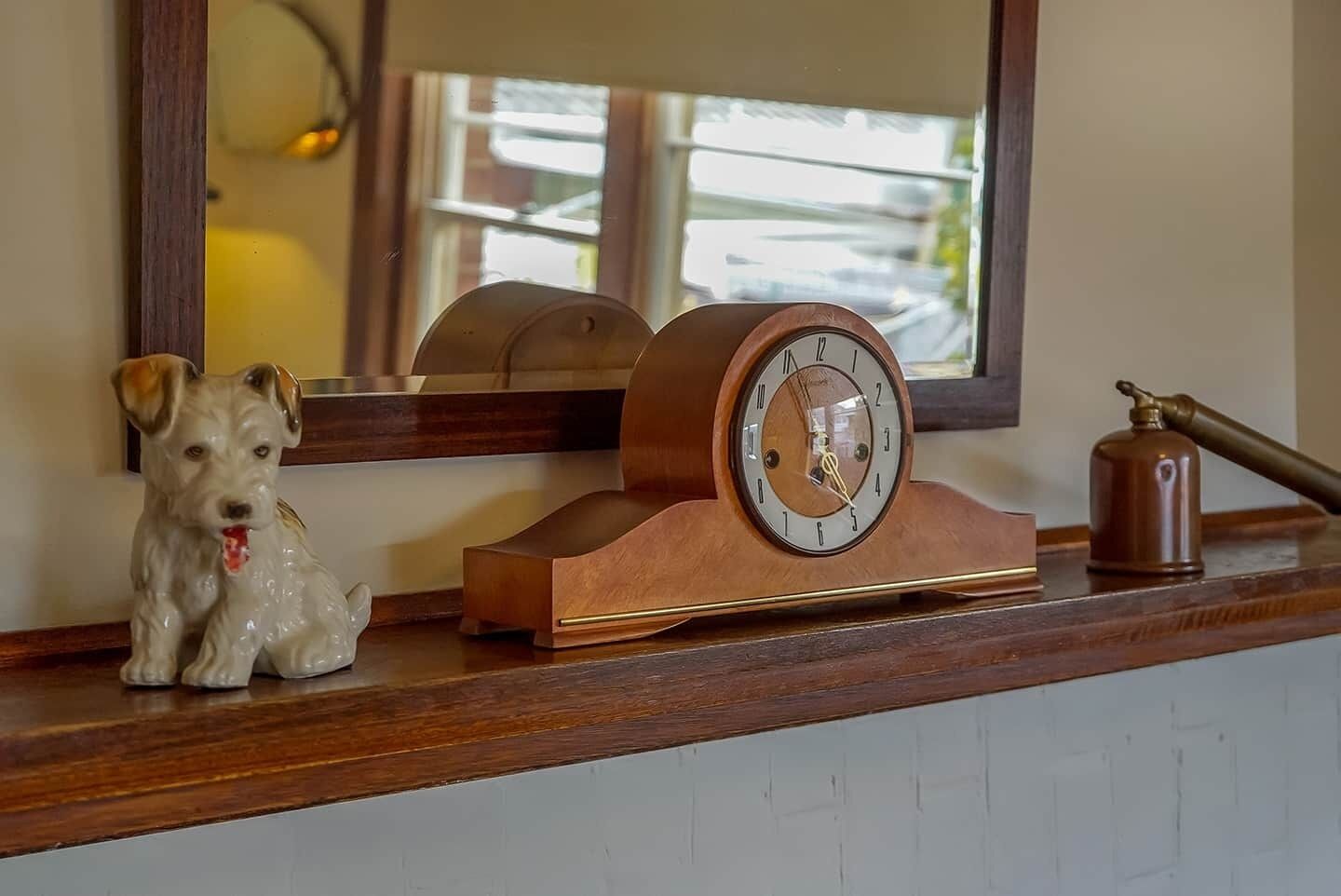 Une étagère en bois avec une horloge, une figurine de chien et une cloche.