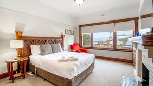 Hotelkamer met een groot bed, een houten hoofdbord, een rode stoel, een openhaard en een groot raam met uitzicht.