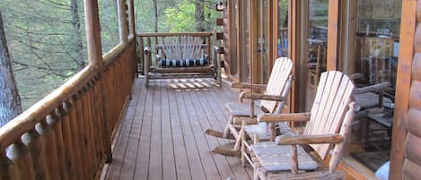 A wooden deck with rocking chairs and a bench, overlooking a forested area.