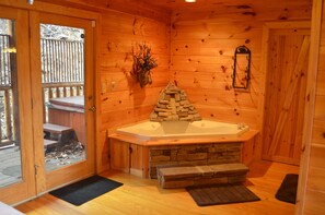 Una baita di legno con camino in pietra, una panca di legno e una porta vetrata che dà sull'esterno.
