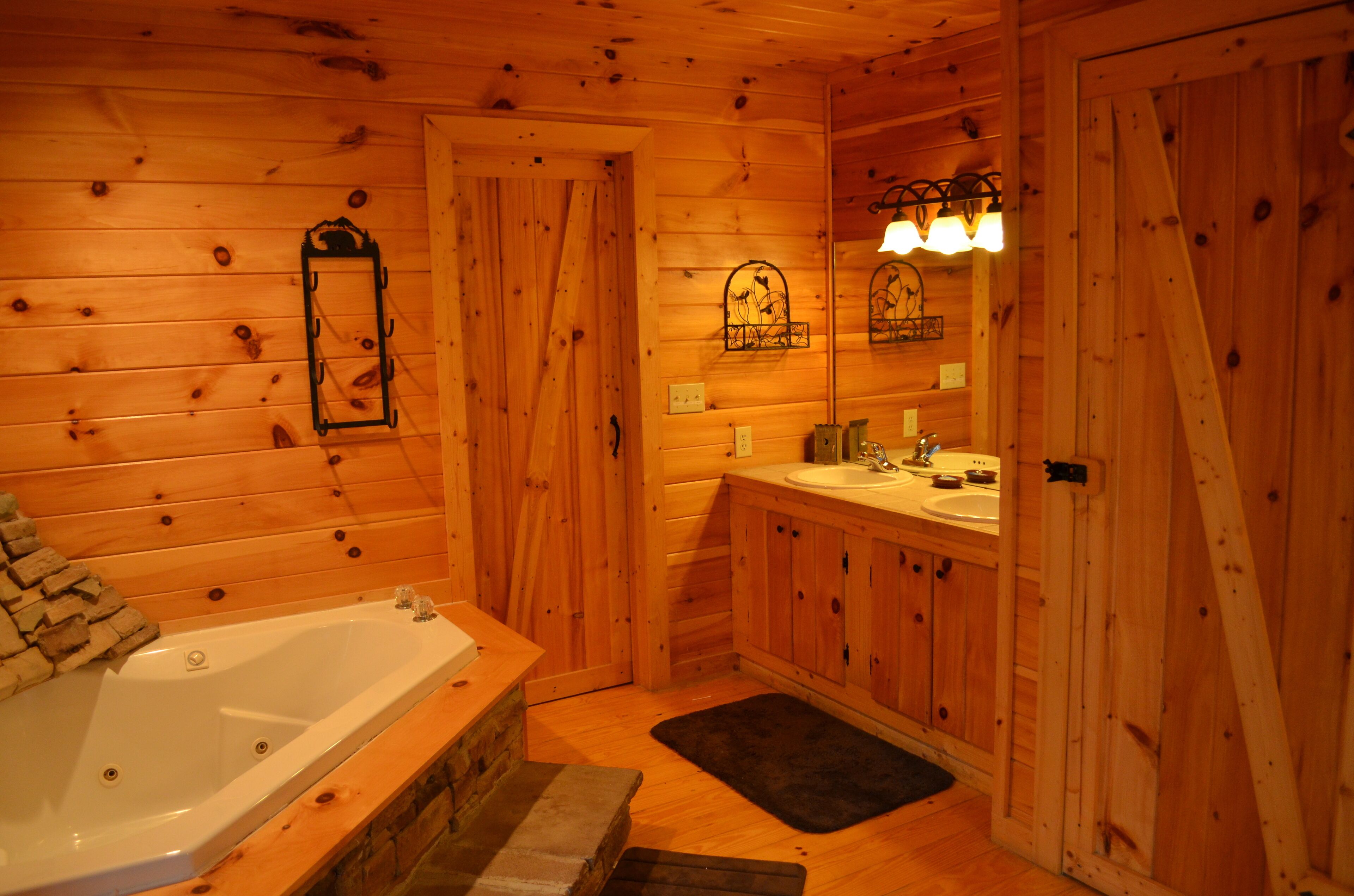 Une salle de bain rustique, avec des murs en bois, comprenant une baignoire, un lavabo et un miroir avec éclairage intégré.