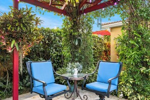 A patio with two blue chairs, a table, and a pergola covered with plants.