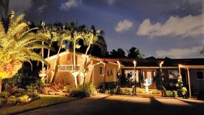 A house with a well-lit entrance, surrounded by palm trees and a garden. - Pet Friendly Tropical Studio with Private Kitchen and Bath (Oakland Park)