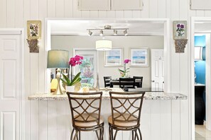 A kitchen with a marble countertop, two chairs, a dining table, and a hanging light fixture.