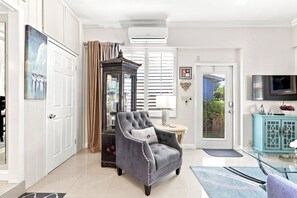 A well-lit living room with a grey armchair, a glass coffee table, and a teal cabinet.