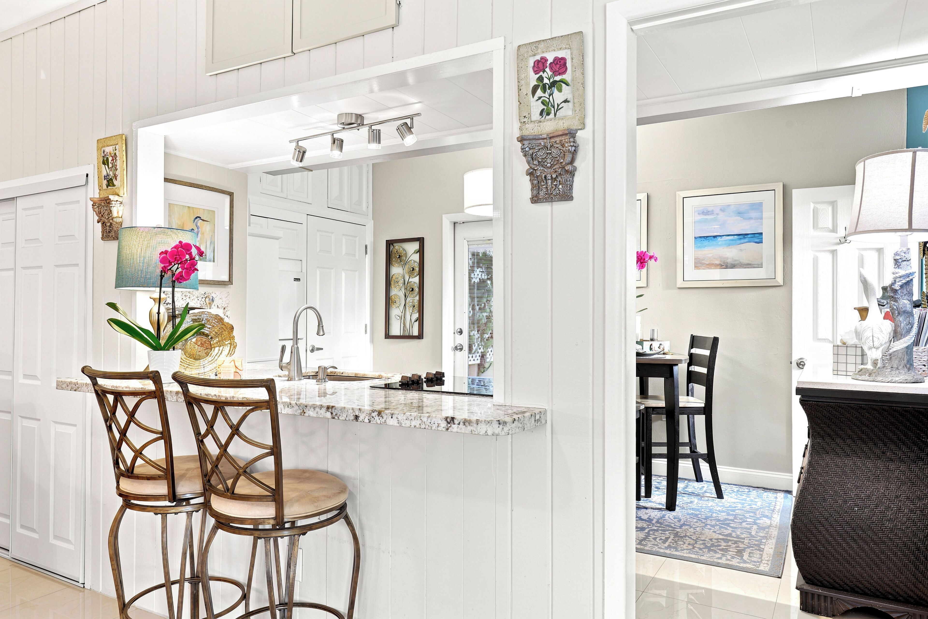 A kitchen with a central island, bar stools, and a dining area with chairs and a table.