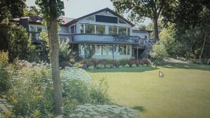 Une maison à deux étages dotée d’un grand porche à l’avant, entourée d’arbres et d’une pelouse bien entretenue.