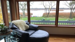 Une pièce avec un canapé en cuir, une table basse en verre et une vue sur un lac et des arbres, visible à travers de grandes fenêtres.
