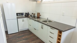 A modern kitchen with white cabinets, a stainless steel sink, and a microwave. - Luxury county guesthouse-continental breakfast supplied/own farm free range eggs (Omarama)