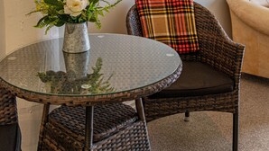 A wicker chair with a plaid cushion, a glass table with a flower vase, and a framed picture on the wall. - Luxury county guesthouse-continental breakfast supplied/own farm free range eggs (Omarama)