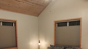 A bedroom with a bed, a ceiling fan, and two windows with blinds.