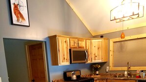 A cozy living room with a brown sofa, patterned pillows, a kitchen with wooden cabinets, a microwave, and a stove.