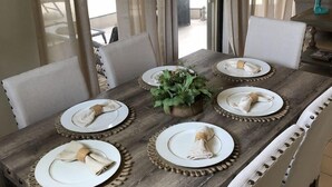 Taula de dinar preparada per a sis, amb plats i gots blancs, i cadires blanques al voltant.