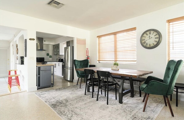 A modern kitchen with a dining area, including a wooden table, chairs, and a clock on the wall.