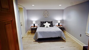 A bedroom with a bed, two nightstands, a wall anchor decoration, and a wooden door. - 1st Street, Cedar Beach Retreat (Saint Augustine)