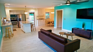 A modern kitchen with built-in appliances, a dining area with a wooden table and chairs, a living room with a sofa and coffee table, and a TV mounted on the wall. - 1st Street, Cedar Beach Retreat (Saint Augustine)