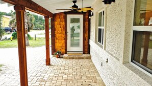 A covered outdoor area with a brick floor, wooden beams, and a ceiling fan. - 1st Street, Cedar Beach Retreat (Saint Augustine)