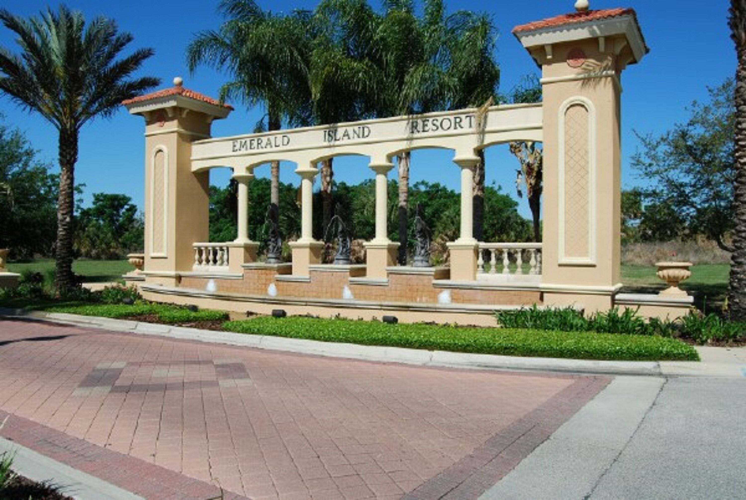 A sign for Emerald Island Resort with a classical architectural design, featuring columns and a fountain.