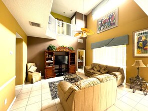A living room with a sofa, a television, a ceiling fan, and a staircase leading to an upper level. - Emerald Island Luxury Castle in Kissimmee,7BR/6BA,3mi to Disney Parks (Kissimmee)
