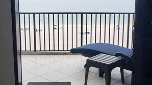 Ein Zimmer mit Blick auf einen Strand durch eine Glastür, eine schwarze Bank und ein gefliesten Boden.