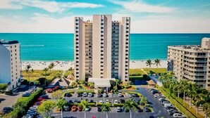 Ein Hochhaus-Hotel mit Parkplatz davor, Strand und blauem Himmel.