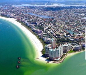 An aerial view of a coastal city with a beachfront, high-rise buildings, and a marina. - Perfect 5th Floor Beachfront condo at Sea Winds. Weekly rentals permitted. (Marco Island)