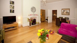 Una sala de estar con televisor de pantalla plana, chimenea, comedor y un sofá rosa intenso.