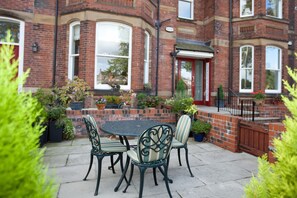 A patio with a round table and four chairs, surrounded by potted plants and a brick wall. - Superb, Ground Floor  City Centre Apartment with private parking for 2 cars (Scarcroft Road York)
