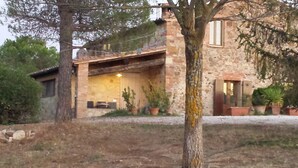 A stone house with a covered patio, potted plants, and a tree in the foreground. - HILLTOP APARTMENT WITH GREAT WIEW BETWEEN SIENA AND VOLTERRA (Casole D'Elsa)