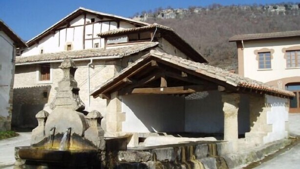Un bâtiment traditionnel en pierre, doté d’un toit en pente et d’une fontaine en pierre dans la cour.