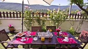 Un espace de restauration en plein air, avec des tables dressées pour le petit-déjeuner, entouré d’une clôture en bois et de verdure.