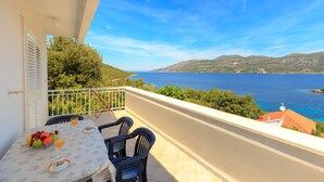 En balkon med et bord dækket til to, der kigger ud over kysten med bjerge i horisonten.
