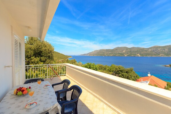 Un balcón con una mesa para dos, con vistas a la costa y montañas al fondo.