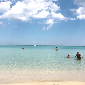 A beach with clear turquoise water, a sandy shore, and a sailboat in the distance. - Patrizia house, independent 10 meters from the sea - San Lorenzo - Reitani - Marzamemi (noto)