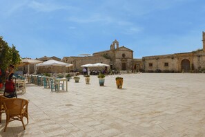 An open courtyard with outdoor seating, a historic building with a bell tower, and potted plants. - Patrizia house, independent 10 meters from the sea - San Lorenzo - Reitani - Marzamemi (noto)