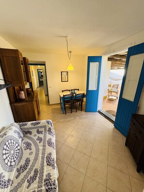 A room with a bed, a dining table with chairs, a blue door, and a view of the outside. - Patrizia house, independent 10 meters from the sea - San Lorenzo - Reitani - Marzamemi (noto)