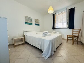 A bedroom with a bed, a chair, a bedside table, and a window with curtains. - Patrizia house, independent 10 meters from the sea - San Lorenzo - Reitani - Marzamemi (noto)