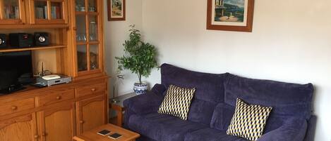A living room with a wooden cabinet, a purple sofa, a small wooden table, and a potted plant.
