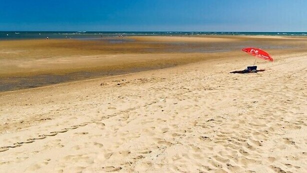 Ein Strand mit einem roten Sonnenschirm und einem Stuhl.