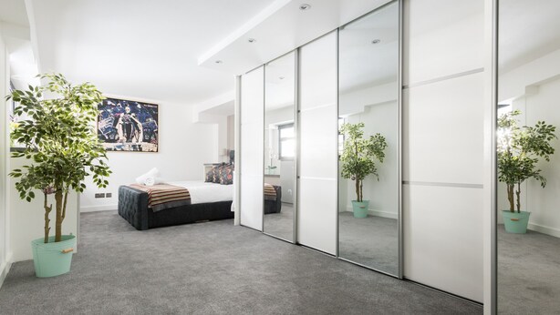 Een moderne slaapkamer met een groot bed, een inloopkast met glazen schuifdeuren en een groot raam.