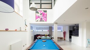 Een moderne woonkamer met een pooltafel, een eethoek en een keuken.
