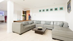 Een moderne woonkamer met een grijze modulaire bank, een houten salontafel en een witte muur met kunstwerken in lijsten.