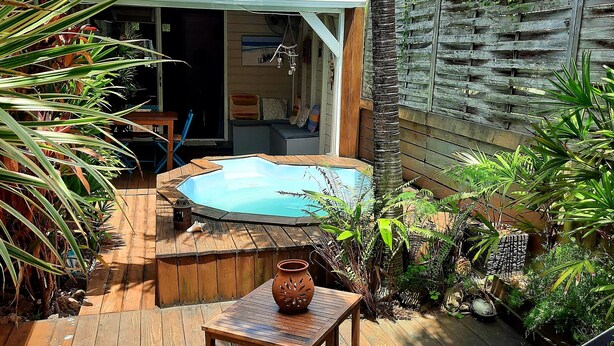 Terraza de madera con jacuzzi, una mesita y sillas reclinables.