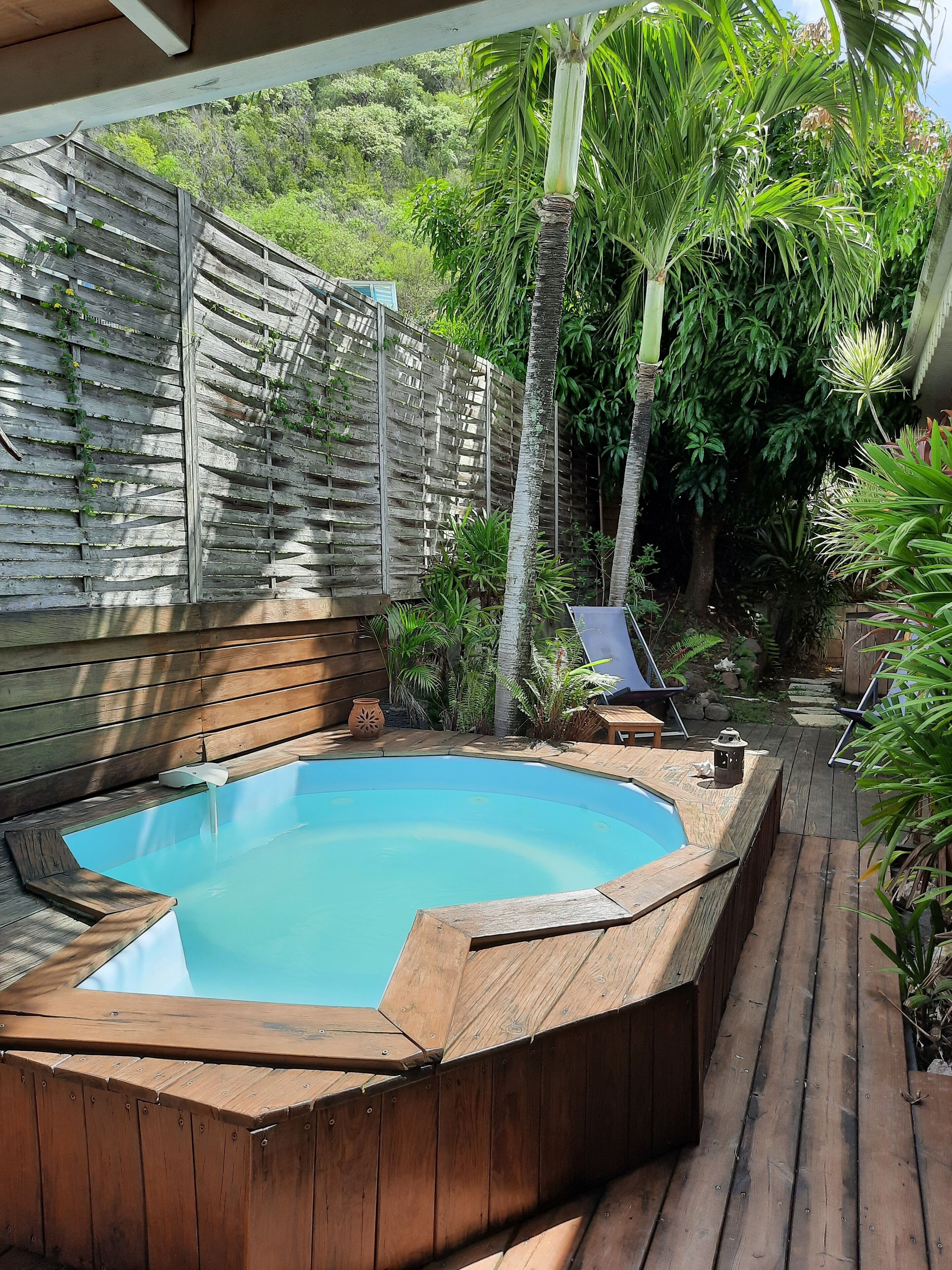 A hot tub surrounded by a wooden deck, with a wooden fence and lush greenery in the background.
